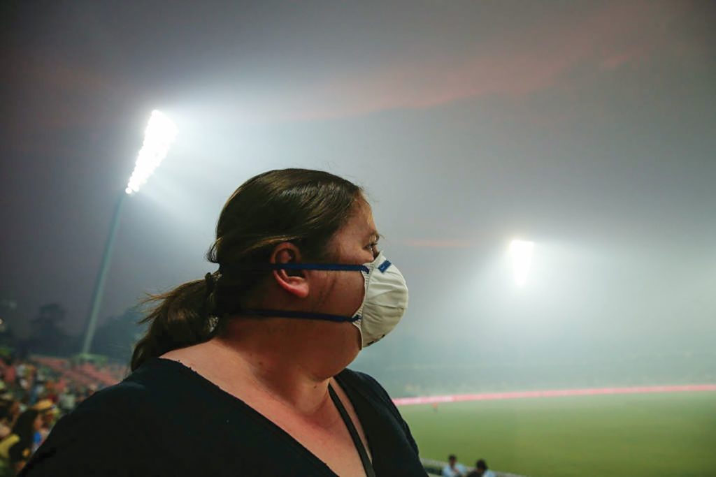 woman with gas mask at cricket with smoke haze around