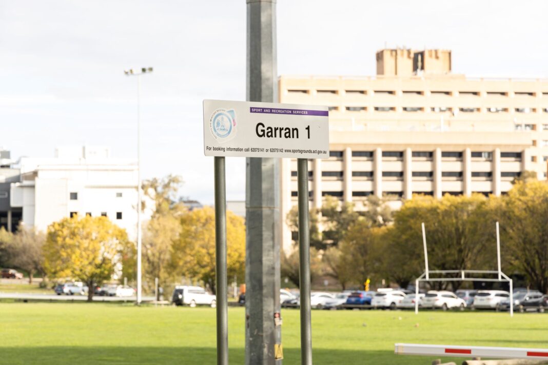 Football oval with Garran oval sign in the foreground and Canberra Hospital in the background