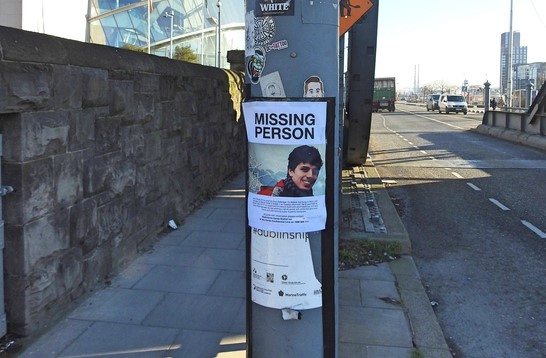 A missing persons poster on a lightpole near a busy street