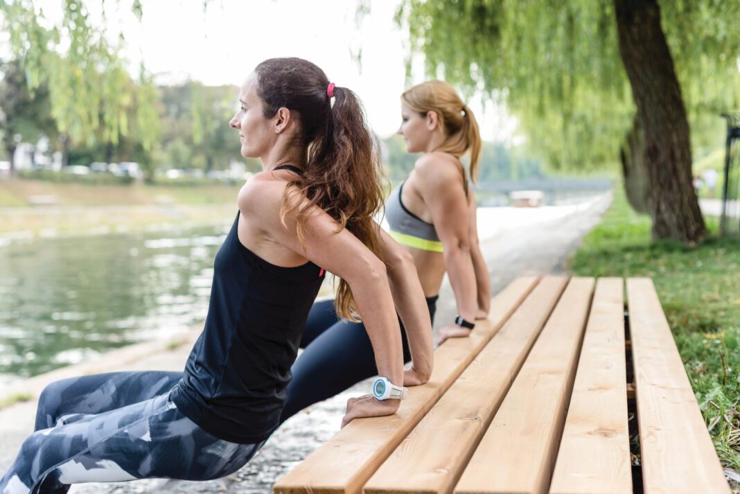 two women stretching on a bench outside