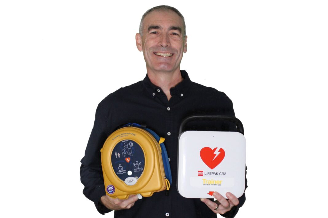Smiling middle aged man holding a yellow defibrillator and a heart health first aid kit