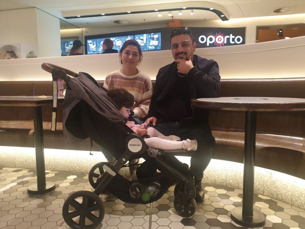 man and woman with a baby in a pram sitting down