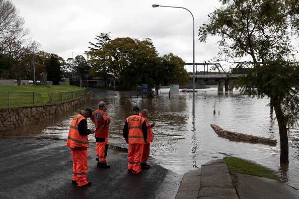 Four emergency service workers in hi-viz gear standing beside a flooded river.