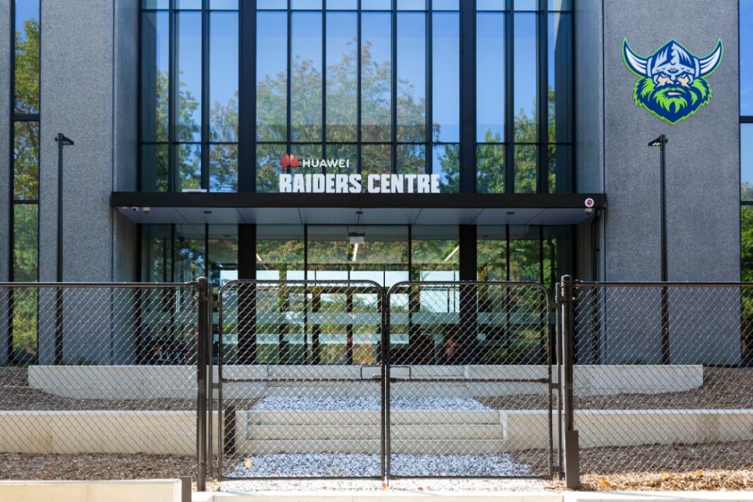 Exterior of entrance to Raiders building with Viking logo on grey wall beside expansive glass frontage