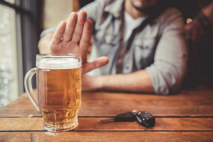 Cropped image of man showing stop gesture and refusing to drink beer. Car keys lying near.