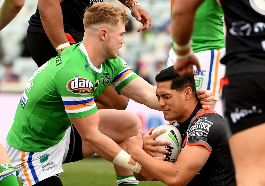 Canberra Raiders football player in green jersey tackling a rugby league player in a black jersey who is holding the ball