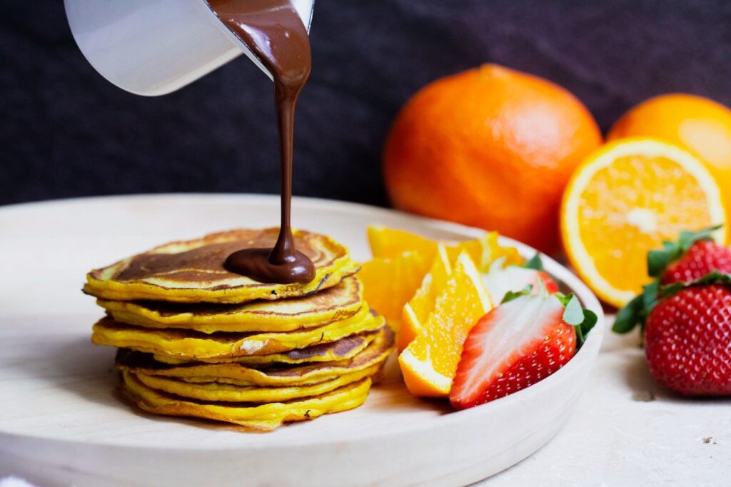 Orange turmeric pancakes with chocolate sauce being poured on top