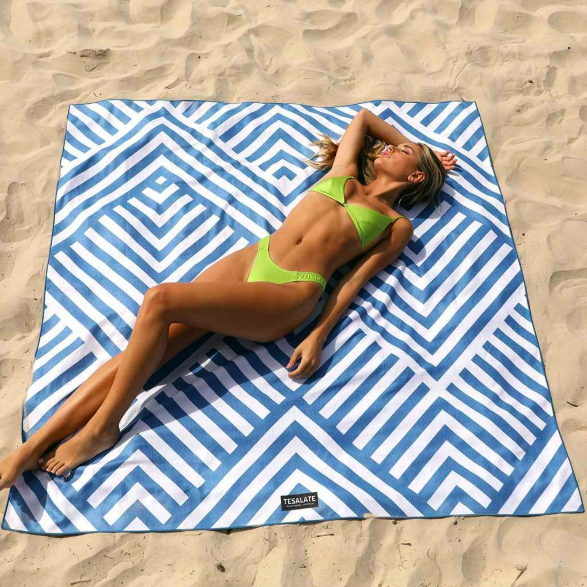woman laying on a blue and white towel on sand