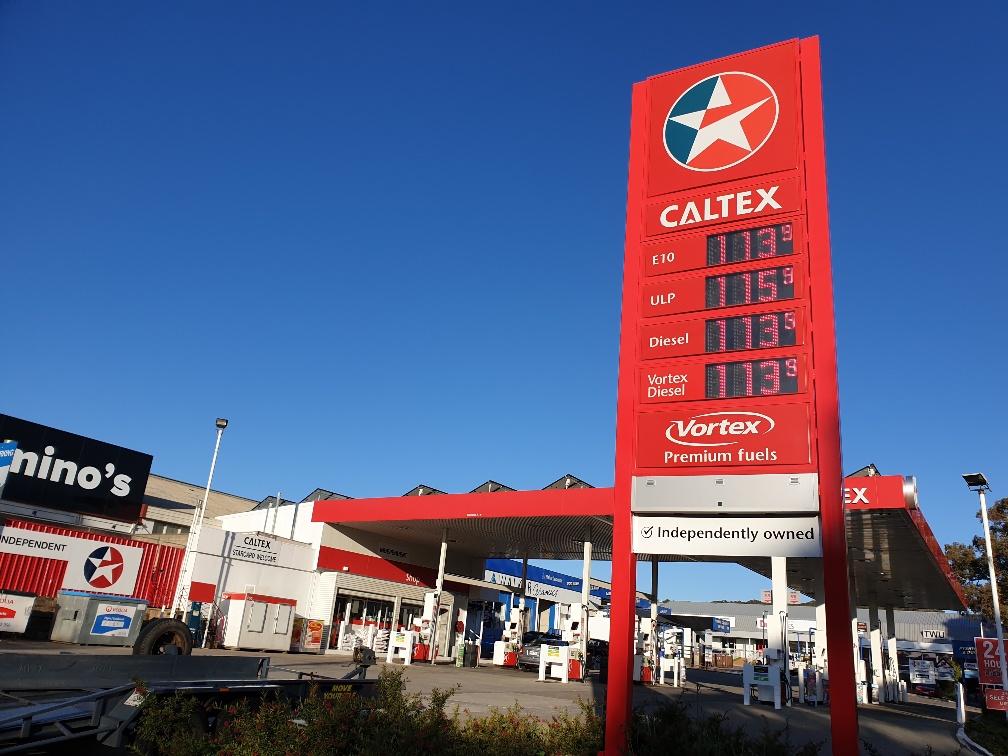 Caltex petrol station with big red sign displaying fuel prices set against a bright blue sky