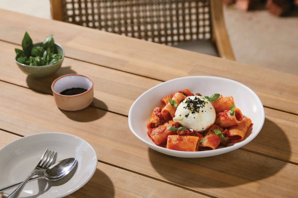 Paccheri pasta with eggplant, tomato and burrata in a bowl on a wooden table