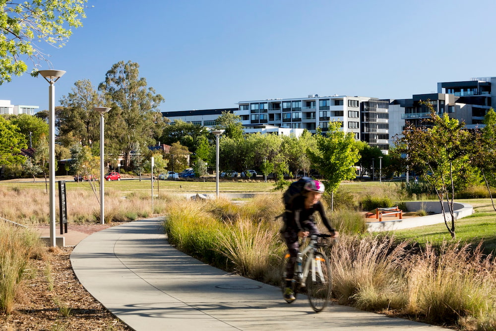 Cyclist riding along path through parklands in front of medium density housing