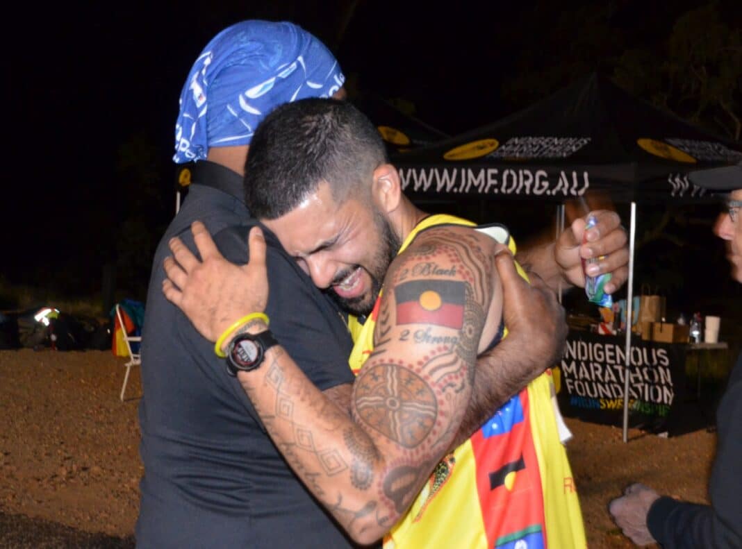 Two Aboriginal Australian men hugging at marathon finish line