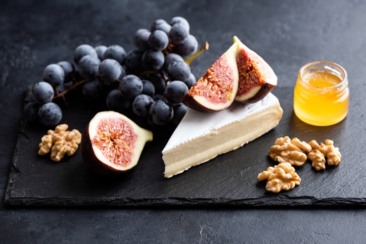a cheese board with brie, figs, grapes and honey