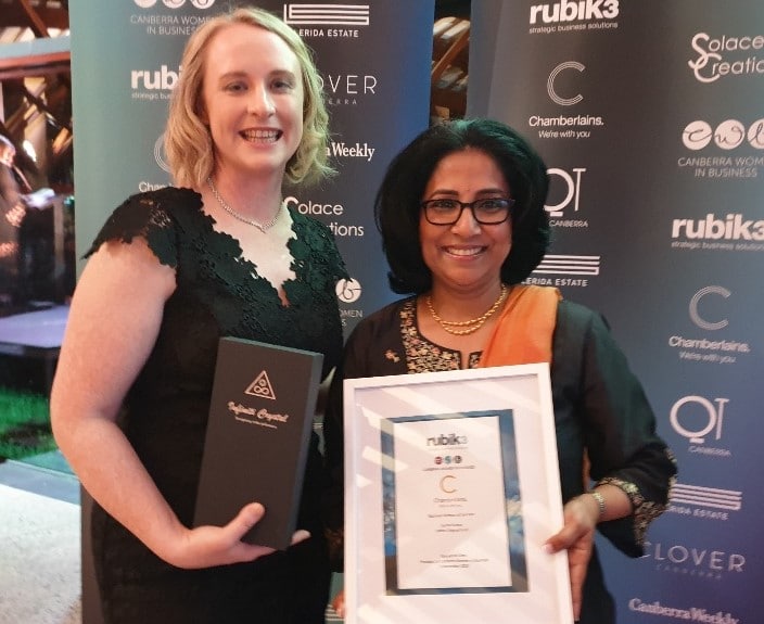 Two women at awards night holding certificate and trophy