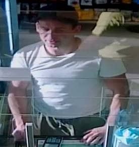 CCTV image of man in white t-shirt at shop counter paying by card