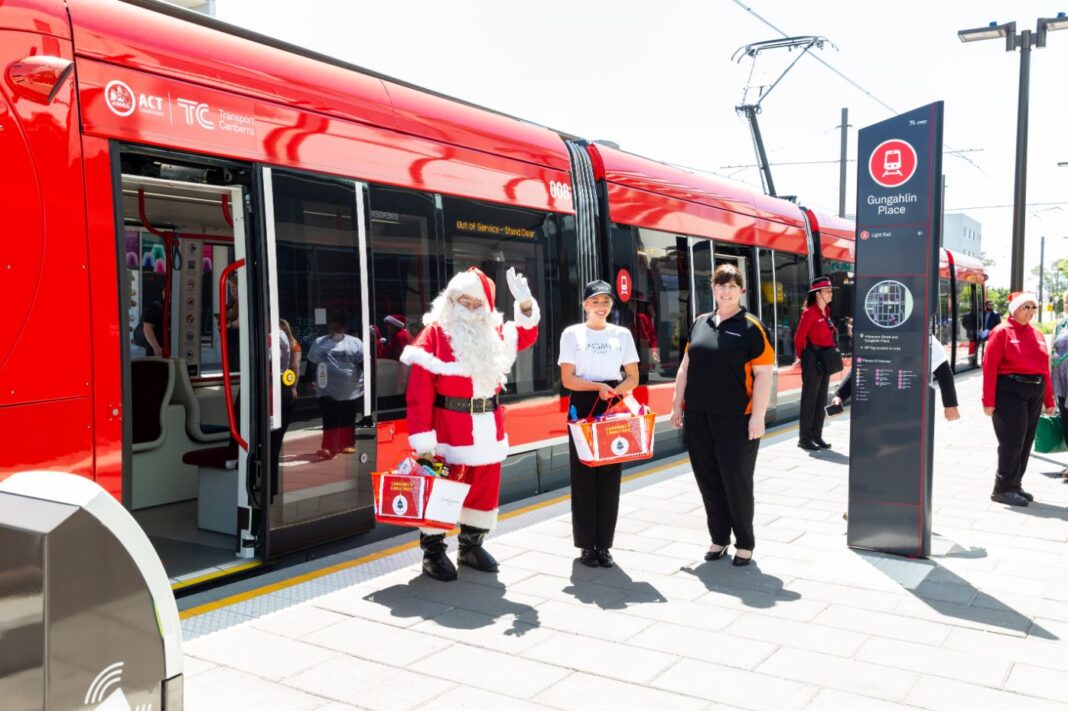 Santa and helpers standing on a tram platform near a red light rail vehicle