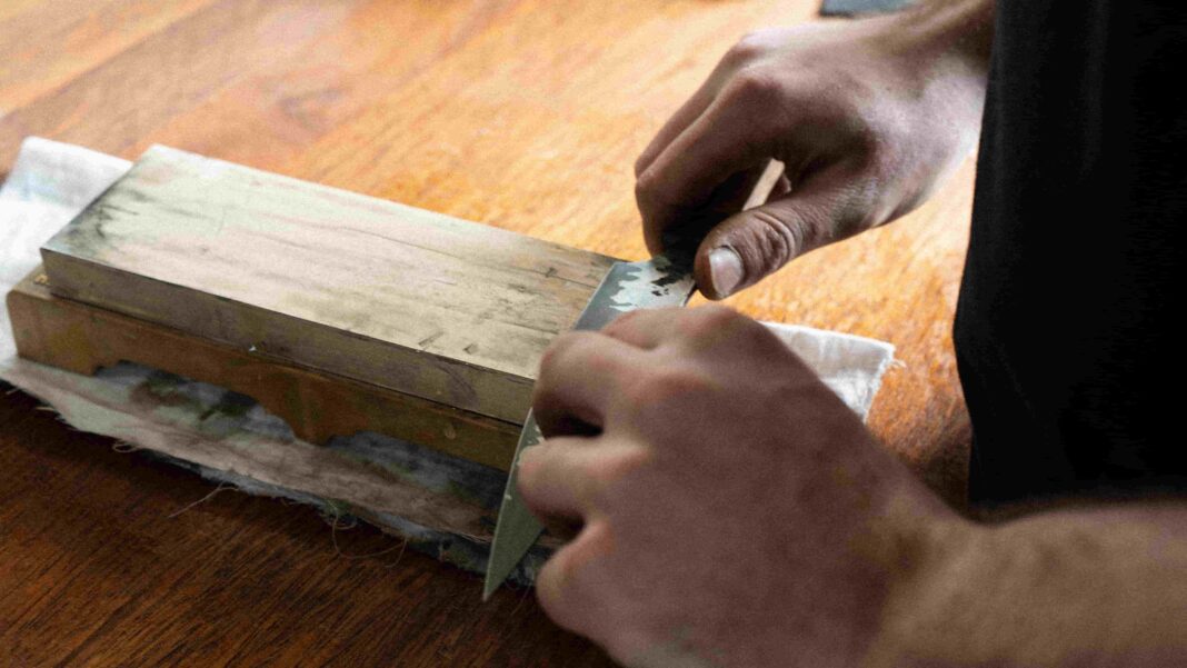 two hands sharpening a knife on a block