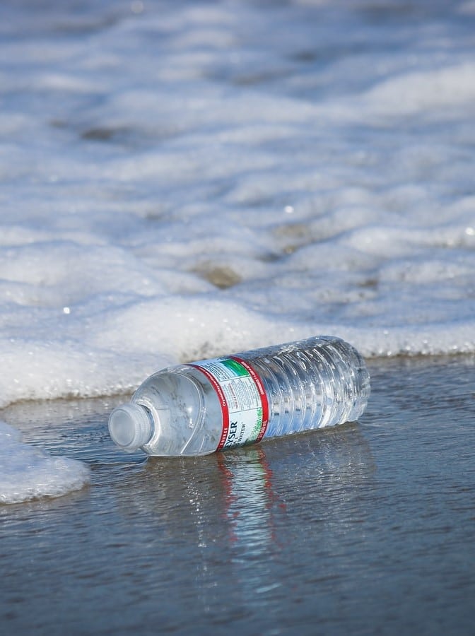 A single-use bottle lies on the beach surrounded by sea foam. Single-use is nominated as Word of the Decade. 