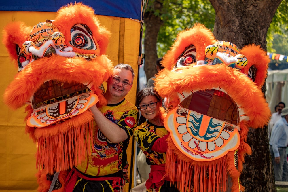 A man and a woman from a lion dance troupe hold their costumes and smile, celebrating Lunar New Year in Canberra.