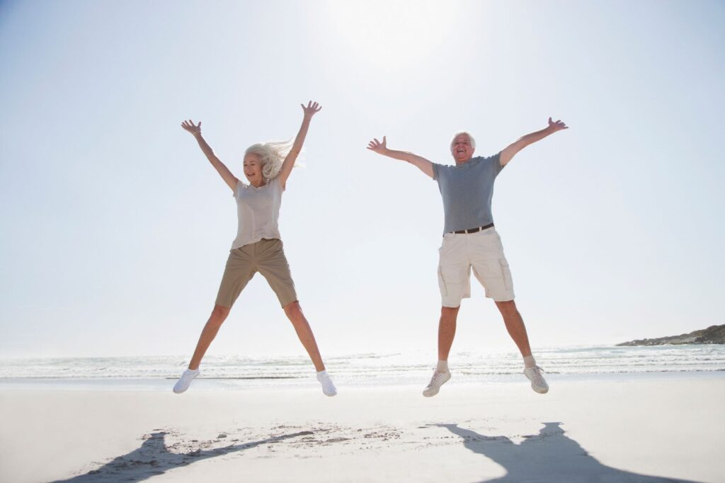 two elderly people jumping for joy on the beach