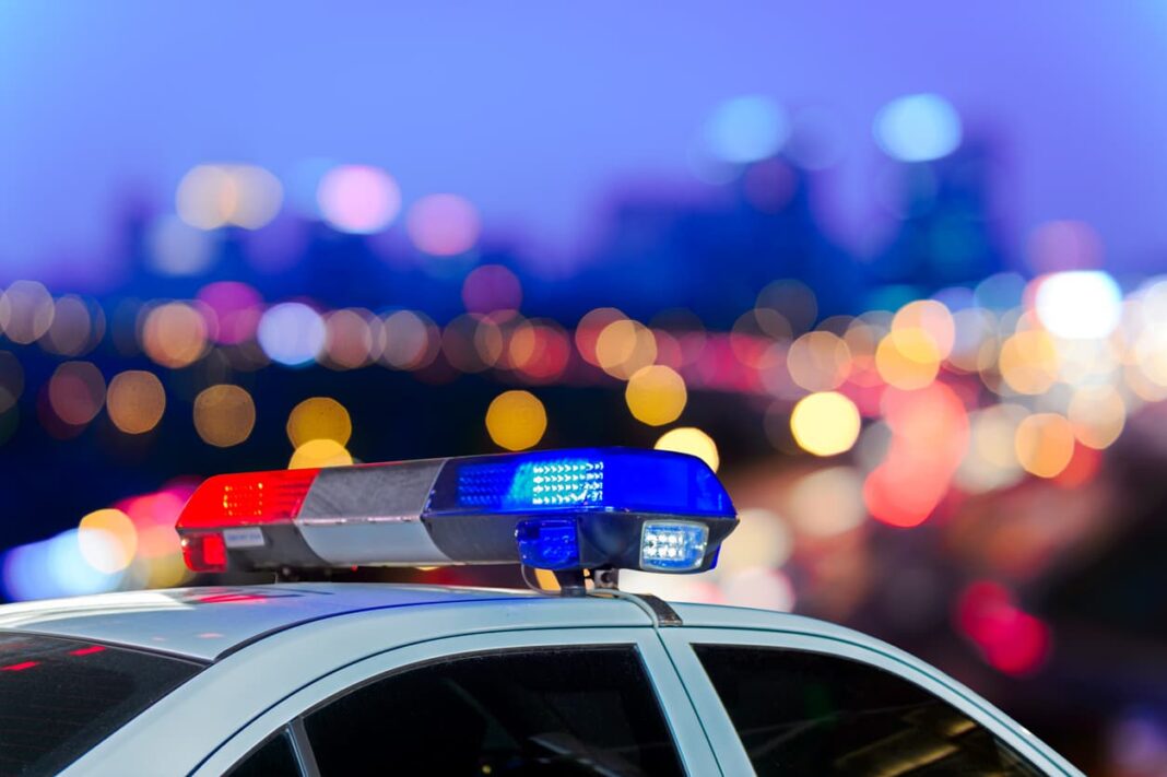 red and blue flashing lights on top of white police car with blurred city lights in background