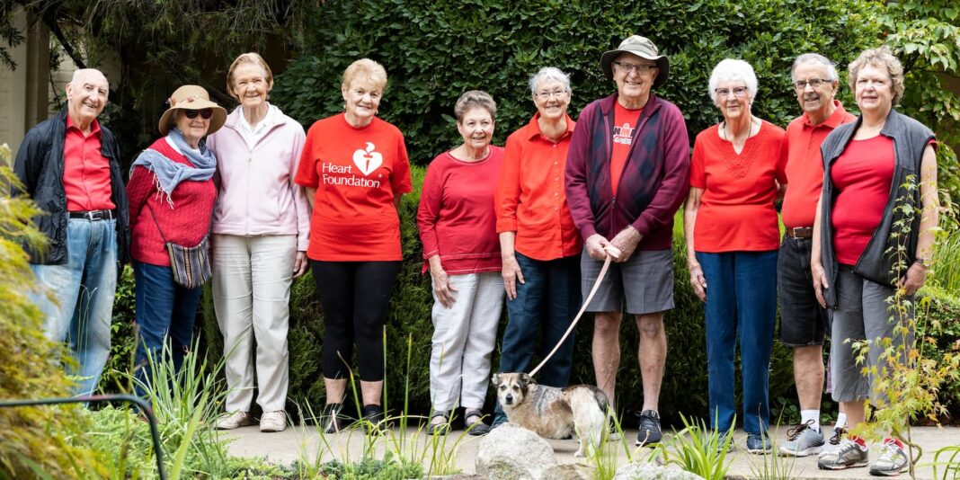 Members of a Heart Foundation Walking group wear red shirts and stand in a line, smiling at the camera