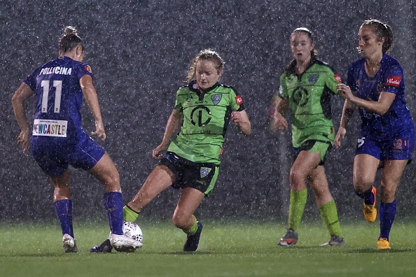 four professional female soccer players, two in green and two in blue, playing football in pouring rain
