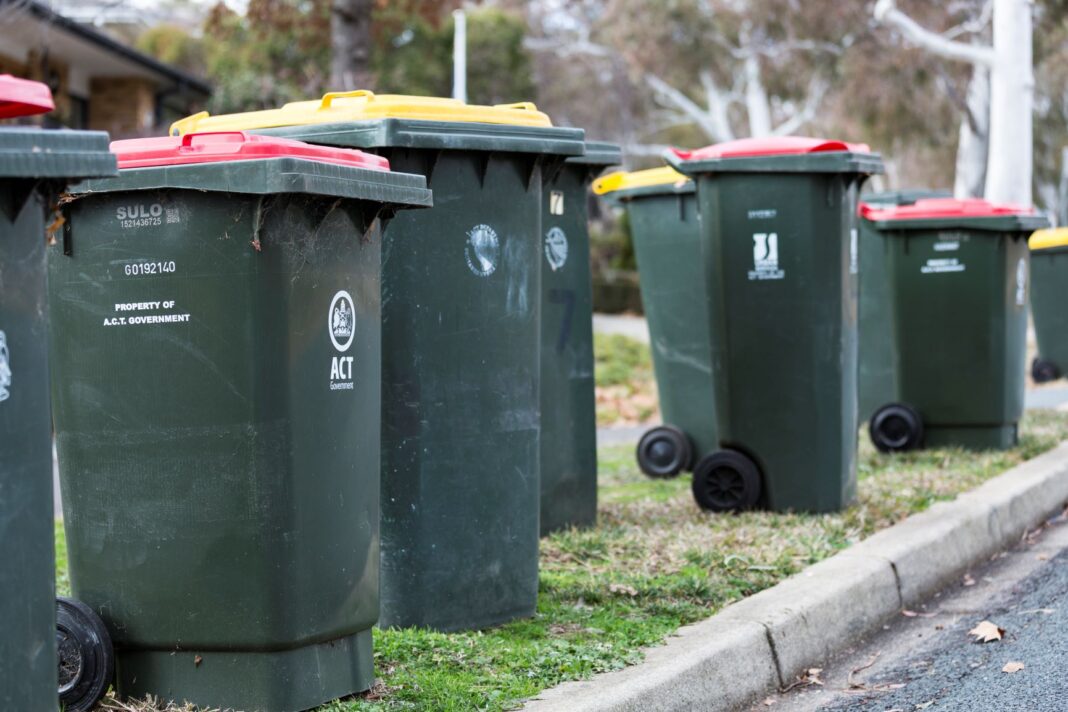 several green wheelie bins with red lids and yellow lids lined up kerbside