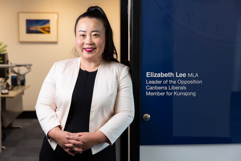 Elizabeth Lee wears a white blazer and a black top with her hair tied in a ponytail, leaning on the entryway to her office; she proposes changing the crimes act to make stealthing illegal