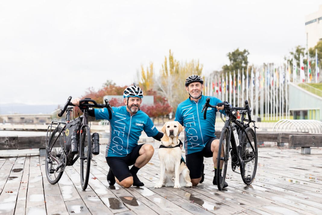 Two cyclists pictured with their bikes and a labrador from Integra Service Dogs