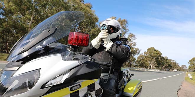 police officer on police motorbike pointing speed gun along the road