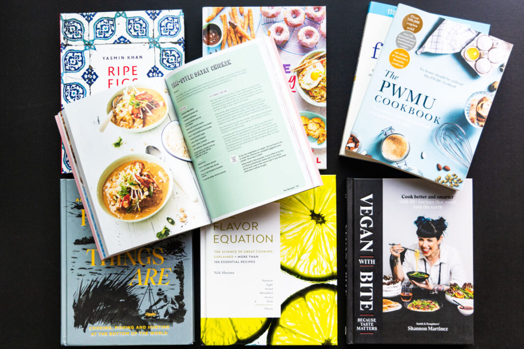 Several beautiful new cookbooks spread across a black tabletop