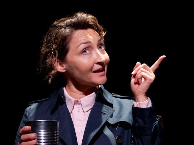 Middle aged female actress with a quizzical expression holding a tin can in one hand and pointing the finger of her other hand