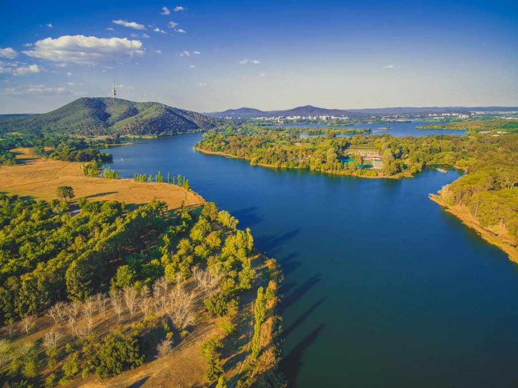 aerial view of Lake Burley Griffin in Canberra surrounded by trees and looking towards Black Mountain Tower on a clear sunny day