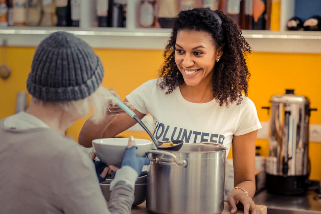 smiling young woman ladling soup to a homeless person holding a bowl
