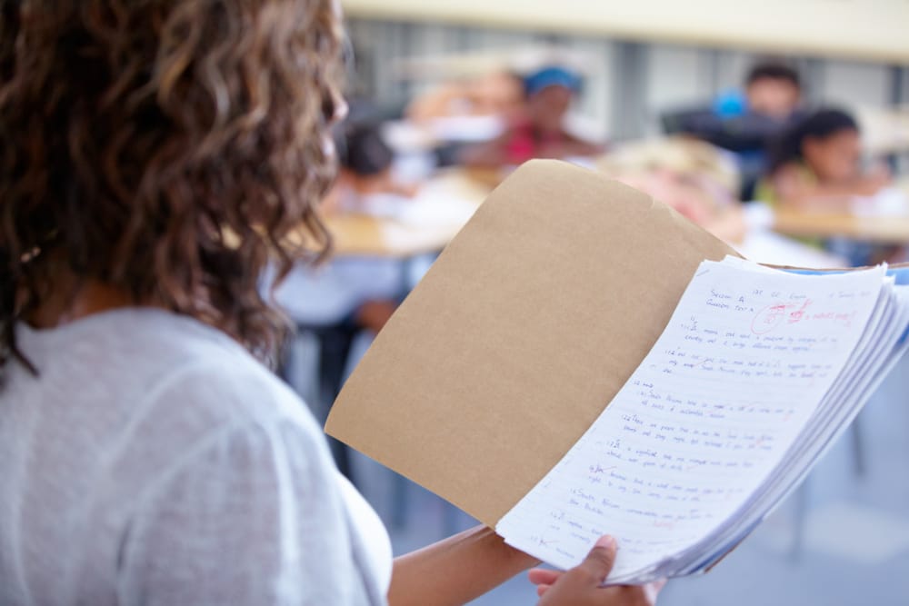 A teacher holding a folder with marked student assignments