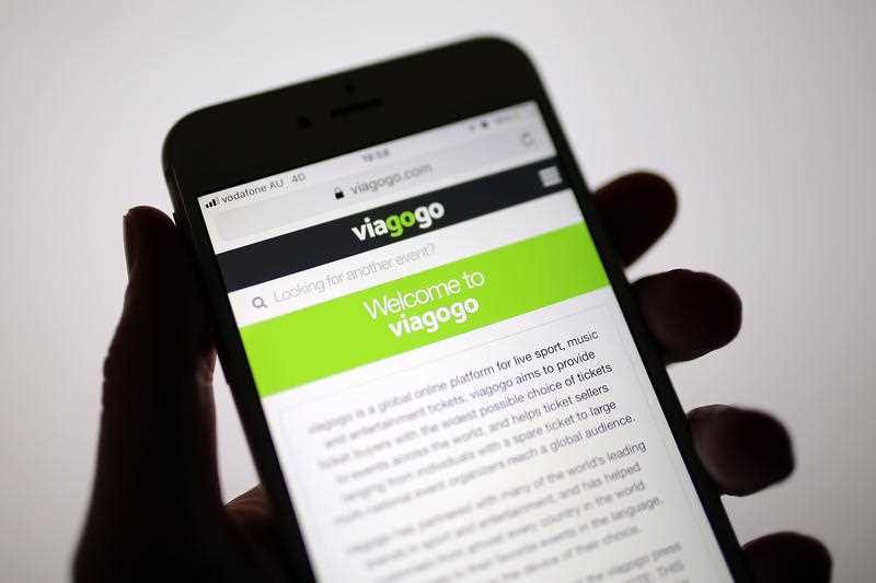 Hand holding mobile phone with Viagogo ticket reselling app displayed on the screen