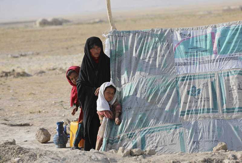 Afghan mother and two children beside makeshift tent in a refugee camp