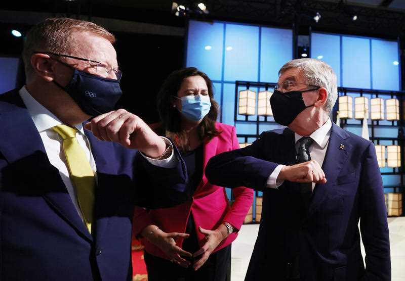 Two middle aged business men wearing masks bump elbows as Queensland Premier Annastacia Palaszczuk looks on, also wearing a face mask