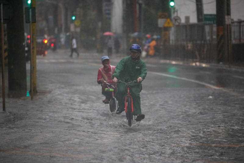 Food delivery riders transit through a flooded road during downpour in Makati, Metro Manila, Philippines