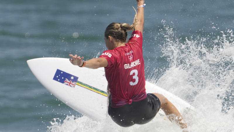 female surfer in red shirt and black shorts on white board riding wave at Tokyo Olympic Games