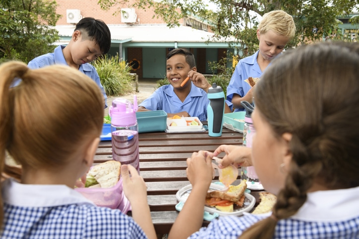 5 school boys and girls sitting at outdoor table outside eating food