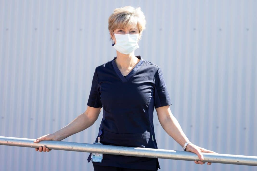 Mature female nurse in dark blue scrubs wearing a white facemask