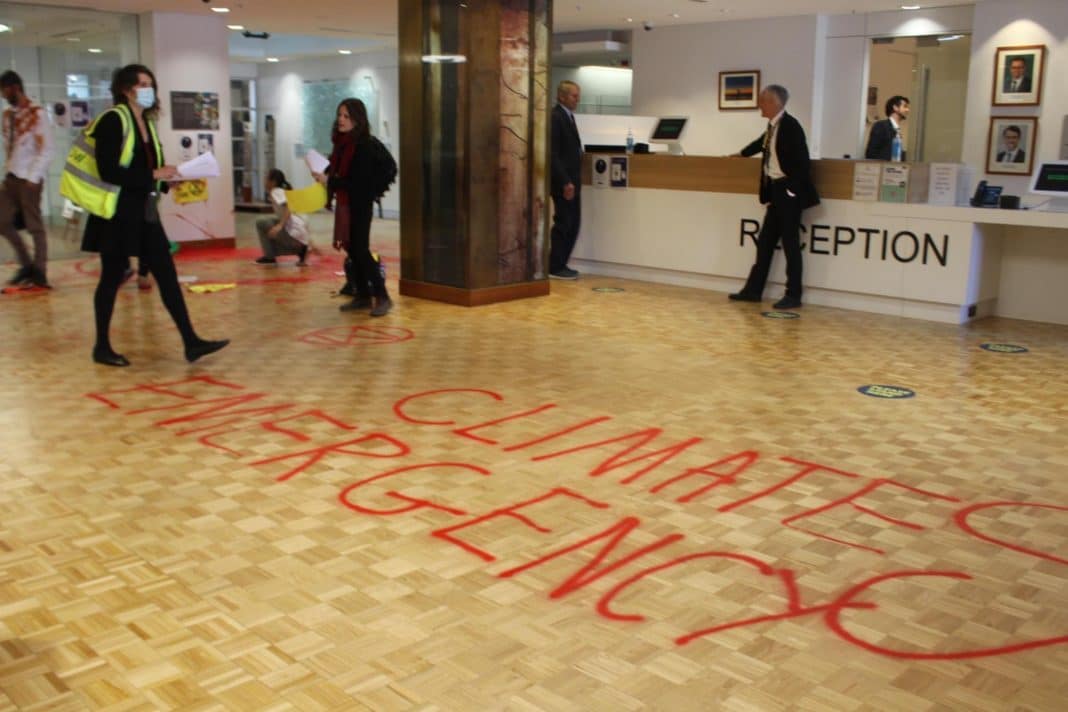 the words 'climate emergency' spray painted in red on the wooden parquetry floor of a government building