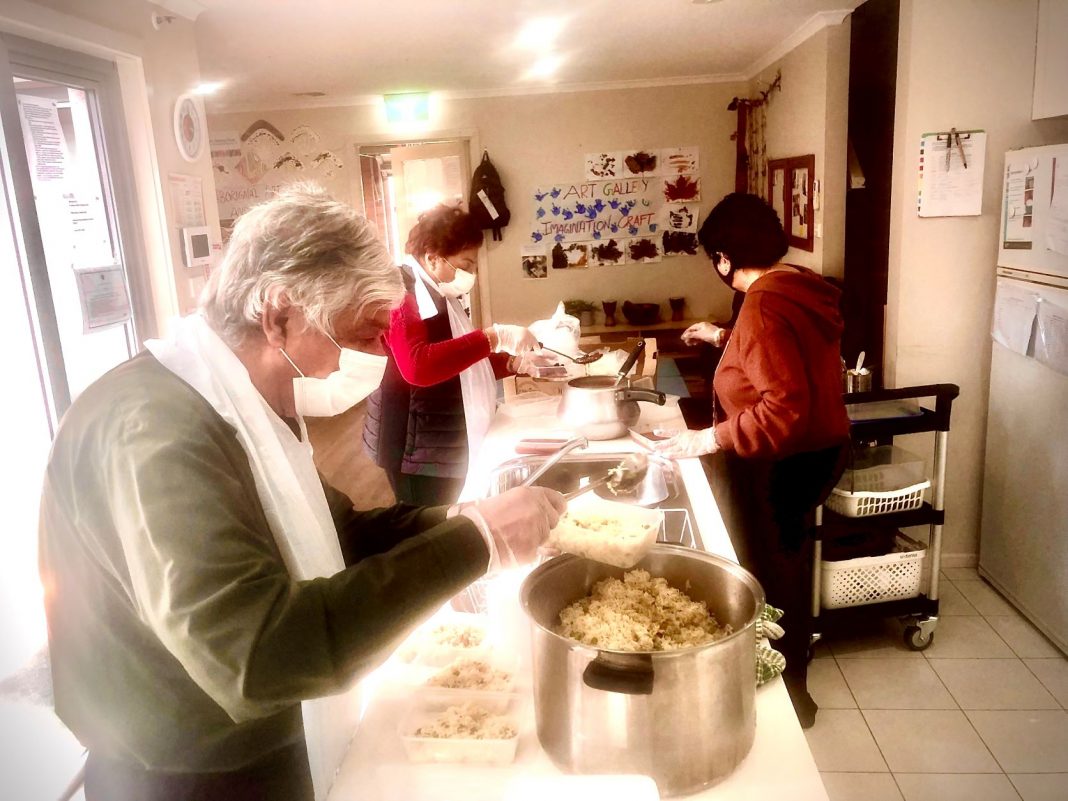 Three people wearing face masks cooking meals in a commercial kitchen
