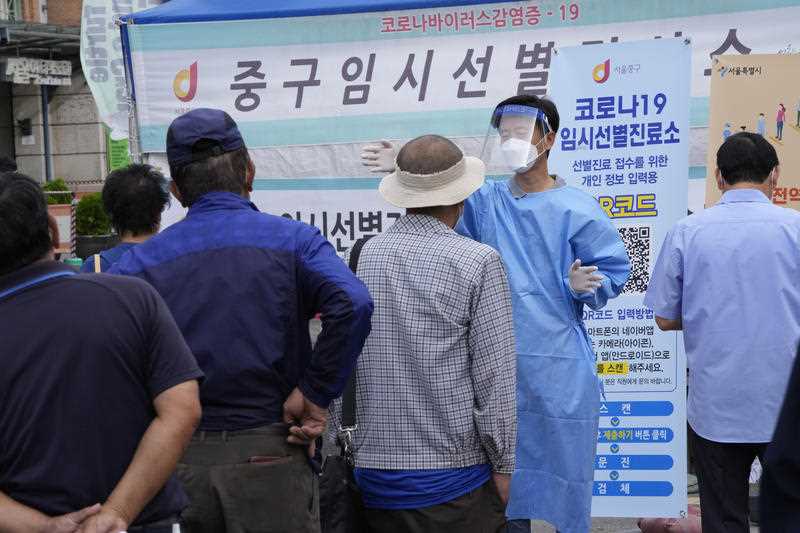 A medical worker guides people as they wait to get coronavirus testing at a makeshift testing site in Seoul, South Korea