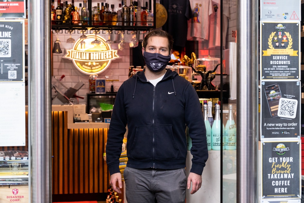 young male business owner in face mask standing in doorway of his eatery and deli in Manuka, Canberra