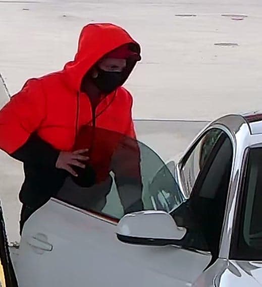 CCTV screen shot of man in red hoodie hopping into white Audi sedan at petrol station
