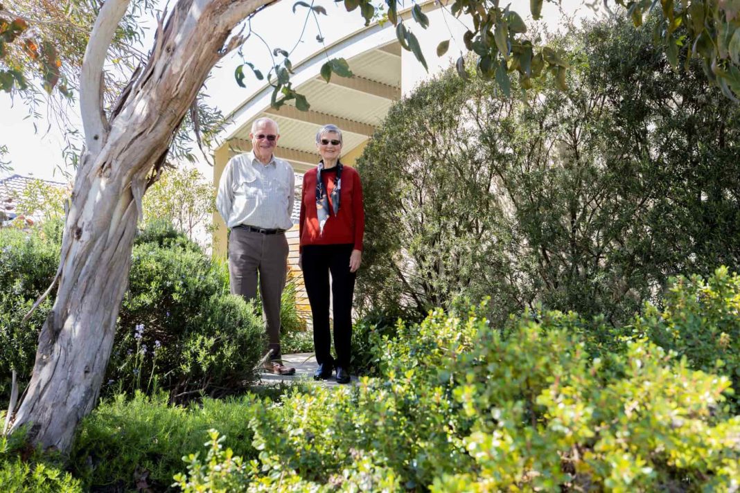 older couple standing in front of sustainable home with Australian native garden
