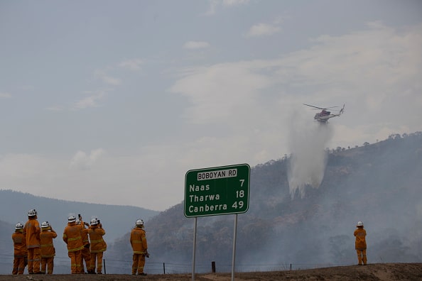 a group of firefighters look on as a helicopter dumps water on a bushfire in the southern parts of the ACT in February 2020